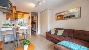A compact living space with a kitchenette, a brown sofa, and a dining area with metal chairs.