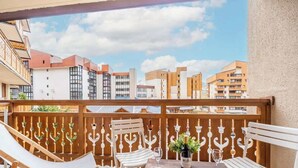 A balcony with white chairs and a table, overlooking a cityscape with various buildings.