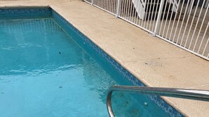 A swimming pool with a metal handrail and a concrete deck. - Beachfront Bliss – Steps to Dining, Shops & More! (Biloxi)