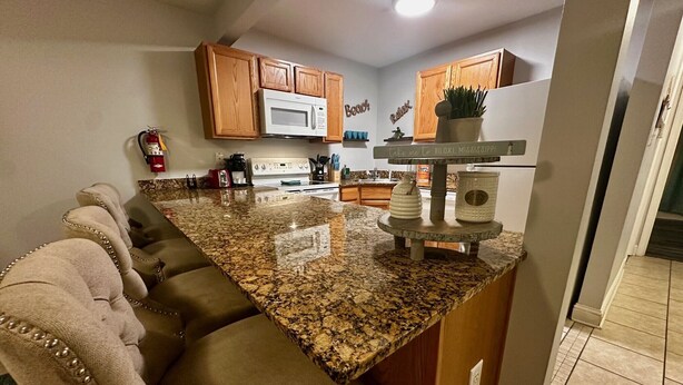 A kitchen with wooden cabinets, a granite countertop, a built-in microwave, and a small island with a plant. - Beachfront Bliss – Steps to Dining, Shops & More! (Biloxi)