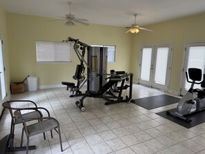 A home gym with exercise equipment, a ceiling fan, and a window with blinds.