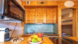 A compact kitchen with wooden cabinets, a built-in oven, and a bowl of fruit on the counter.