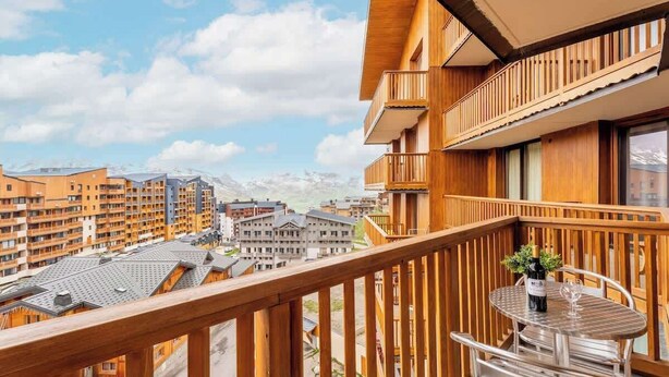 A balcony with a wooden railing, a table, and a bottle of wine.