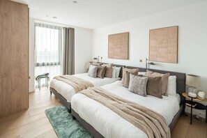 Een moderne slaapkamer met twee bedden, een groot raam met gordijnen en een groen vloerkleed.