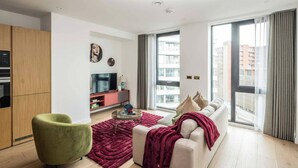 Un salon moderne avec un canapé, un fauteuil vert, une table basse et un téléviseur posé sur un meuble.