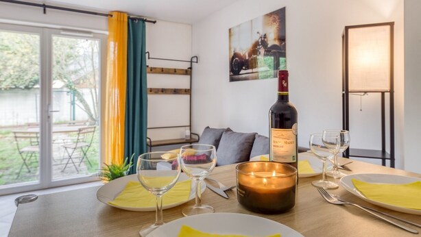 A dining area with a table set for two, a bottle of wine, and a candle. - Cocoon - garden - Key box - Wifi (Baulne)