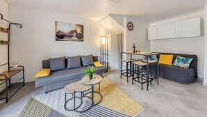 A modern living room with a grey sofa, a coffee table, and a dining area with bar stools. - Cocoon - garden - Key box - Wifi (Baulne)