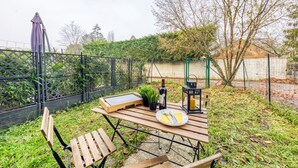 An outdoor dining area with a wooden table, chairs, a bottle of wine, a lantern, and a potted plant. - Cocoon - garden - Key box - Wifi (Baulne)