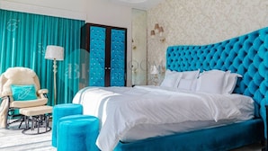 Quarto com uma cama grande, cortinas verde-água, uma poltrona fofinha e um espelho.