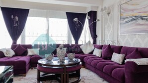 Sala de estar com sofá roxo, mesa de centro redonda e uma grande pintura na parede.