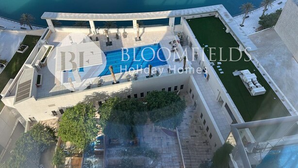 Uma área de piscina no terraço com vista clara para o mar, cercada por edifícios modernos.