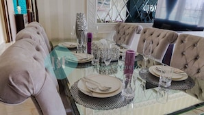 Mesa de jantar para quatro com tampo de vidro, rodeada por cadeiras estofadas.