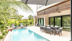 A modern outdoor pool area with lounge chairs and a dining table, surrounded by lush greenery and palm trees. - Lotus Villas #1-Leeward Palms. Your Gateway to Paradise & Step into Serenity.... (Leeward Settlement)