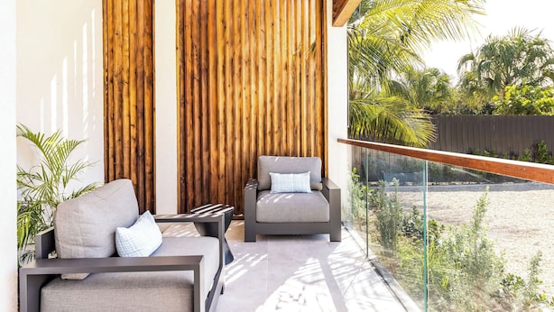 A balcony with two grey sofas, a small table, and a wooden wall. - Lotus Villas #1-Leeward Palms. Your Gateway to Paradise & Step into Serenity.... (Leeward Settlement)