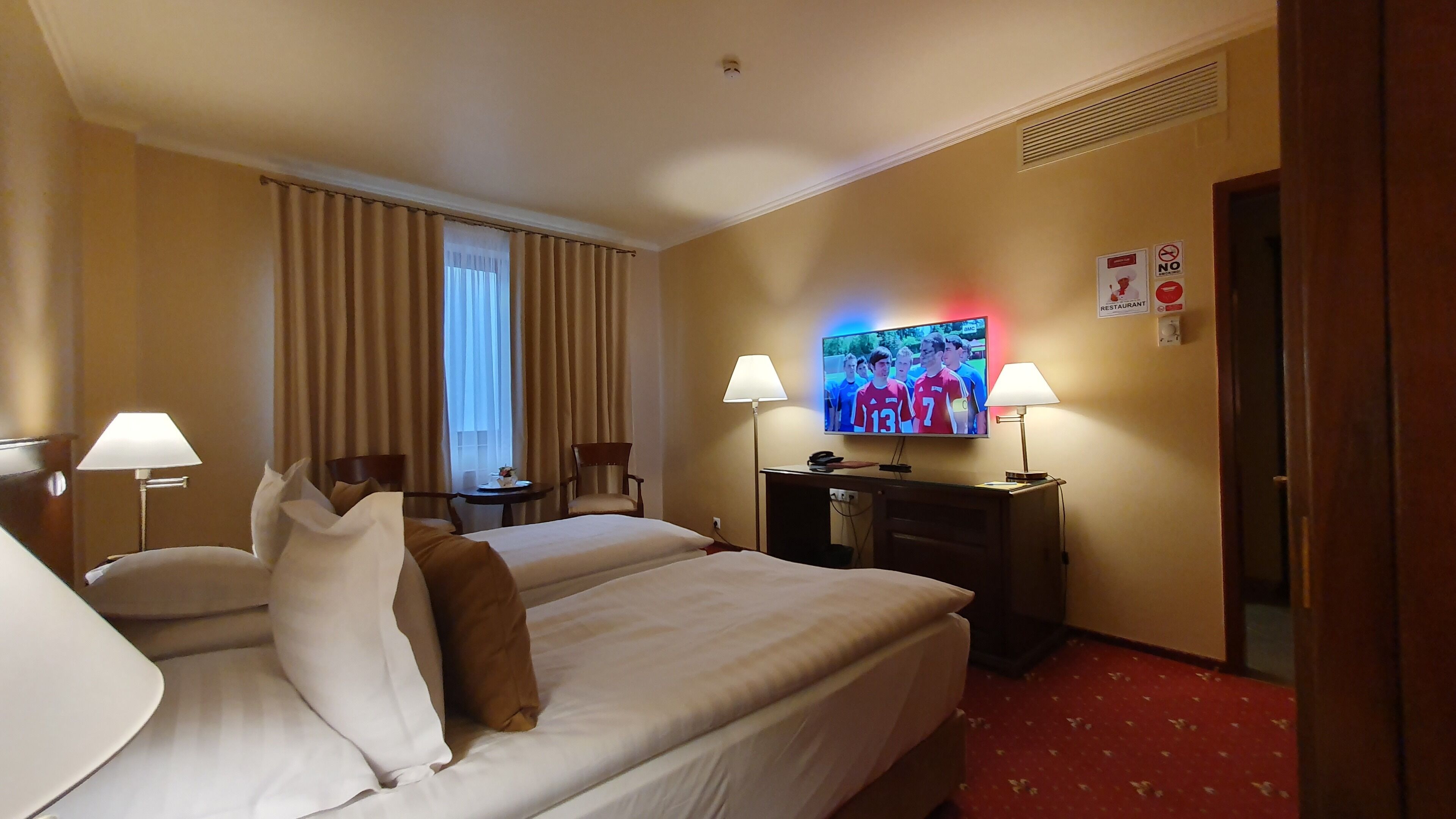 Ein Hotelzimmer mit zwei Betten, einem Fernseher, einem Schreibtisch und einem Sessel.