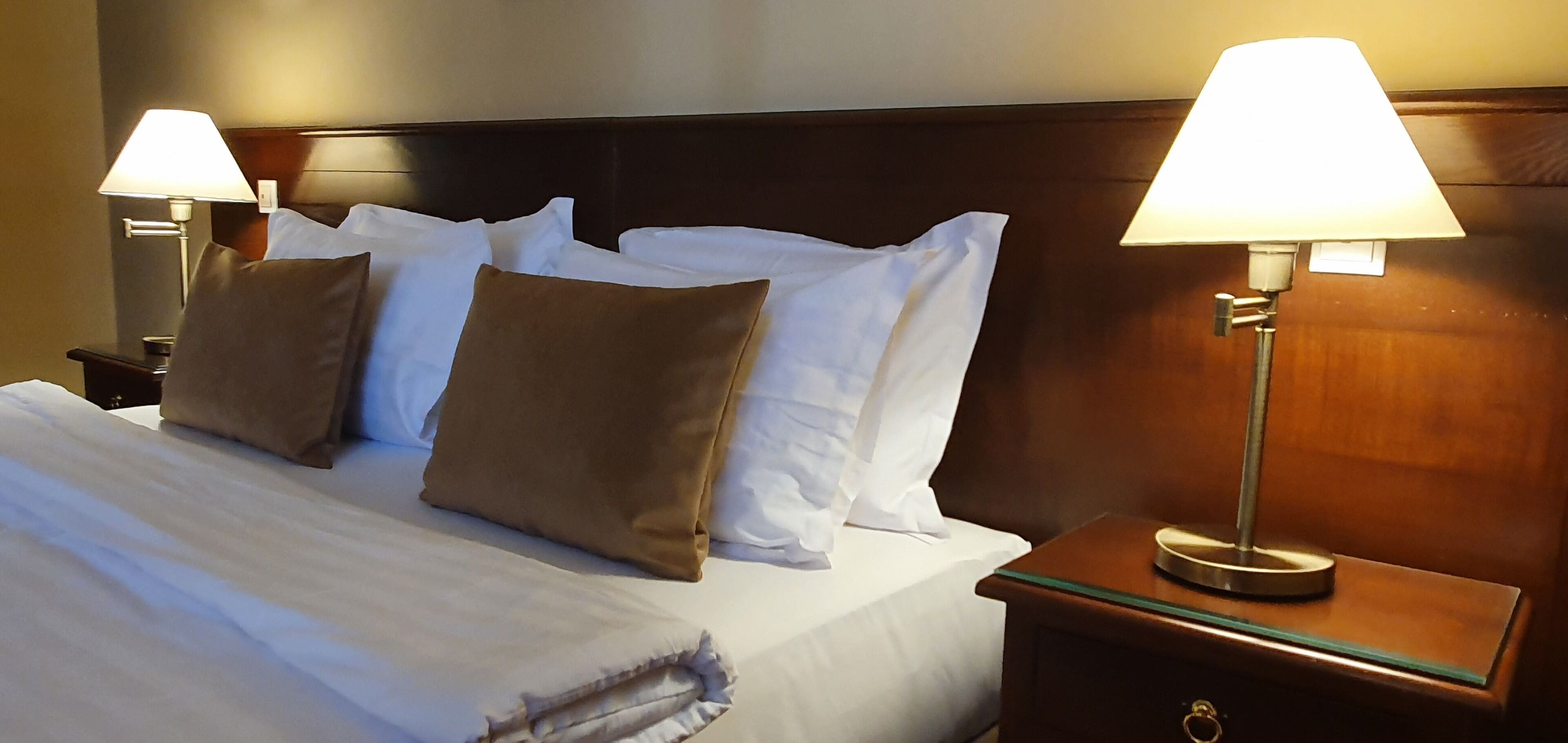 A neatly made bed with white and brown pillows, two bedside lamps, and a wooden headboard.