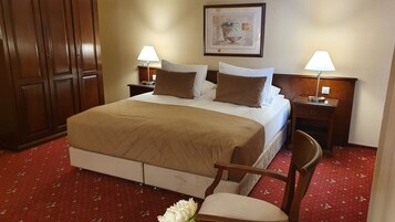 Habitación de hotel con una cama grande, dos mesitas de noche con lámparas, un armario de madera y un cuadro enmarcado en la pared.