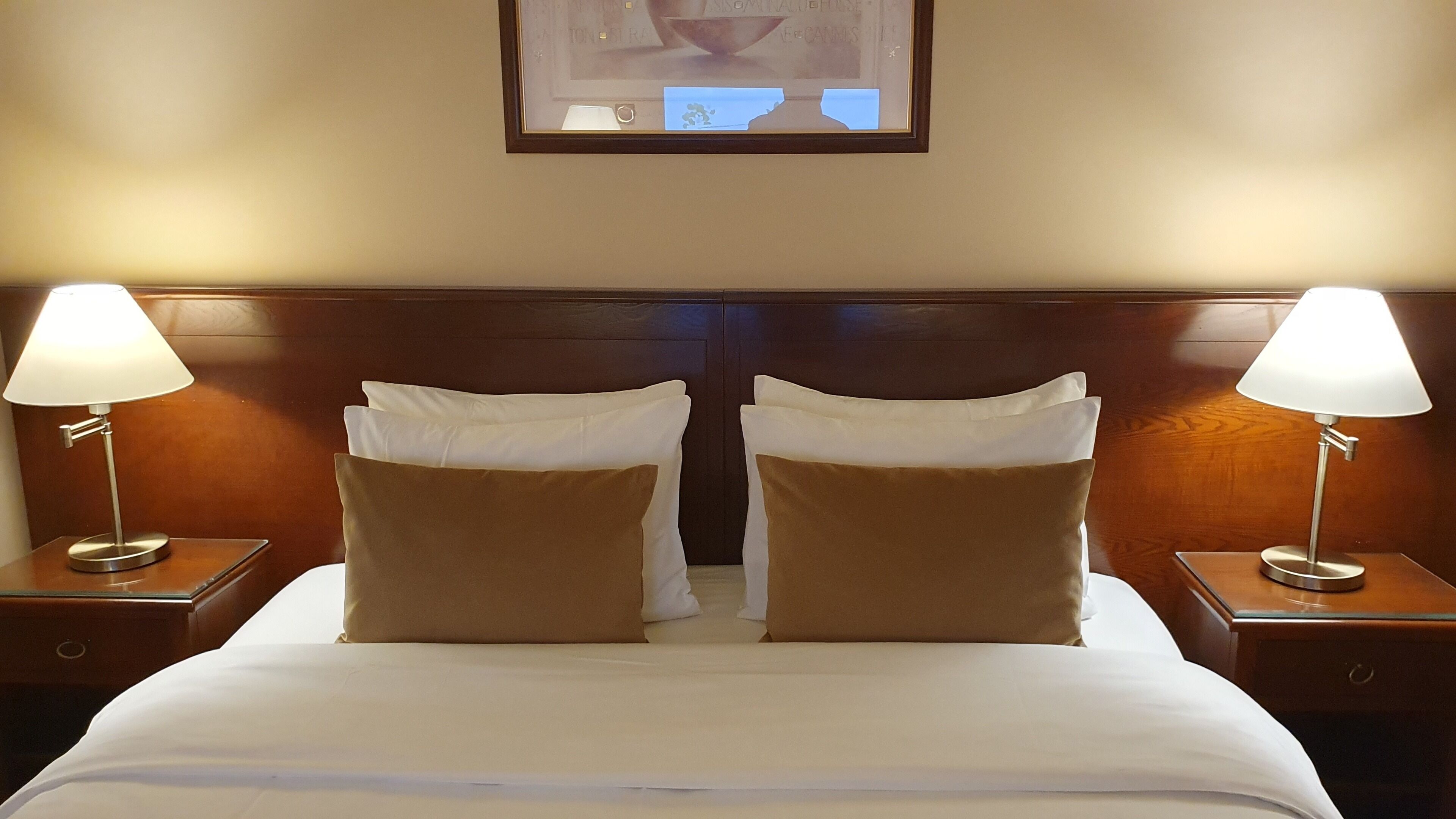 Una cama doble con dos almohadas, cabecera de madera y dos lámparas de noche.