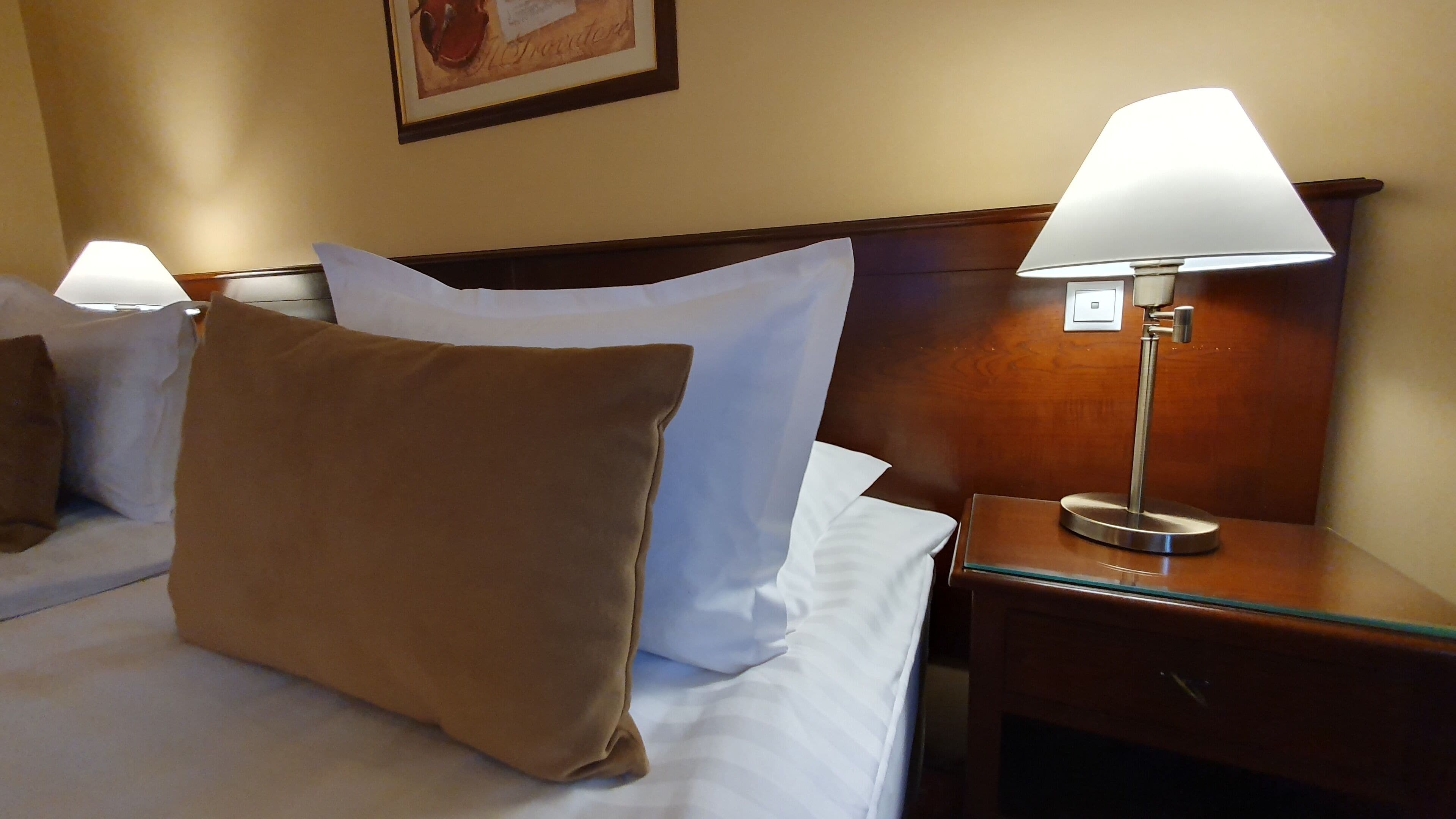 A hotel room with a neatly made bed, a nightstand with a lamp, and a framed picture on the wall.