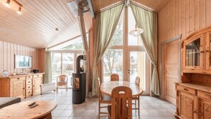 Interior de una cabaña de madera con una mesa de comedor, sillas, chimenea y televisor.