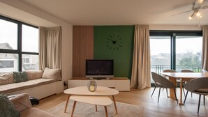 A modern living room with a sofa, a coffee table, a TV, and a dining area with chairs. - Apartment in De Panne Near the Beach (Koksijde)