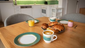 A breakfast table with croissants, coffee, and juice in a modern kitchen with green tiles. - Apartment in De Panne Near the Beach (Koksijde)