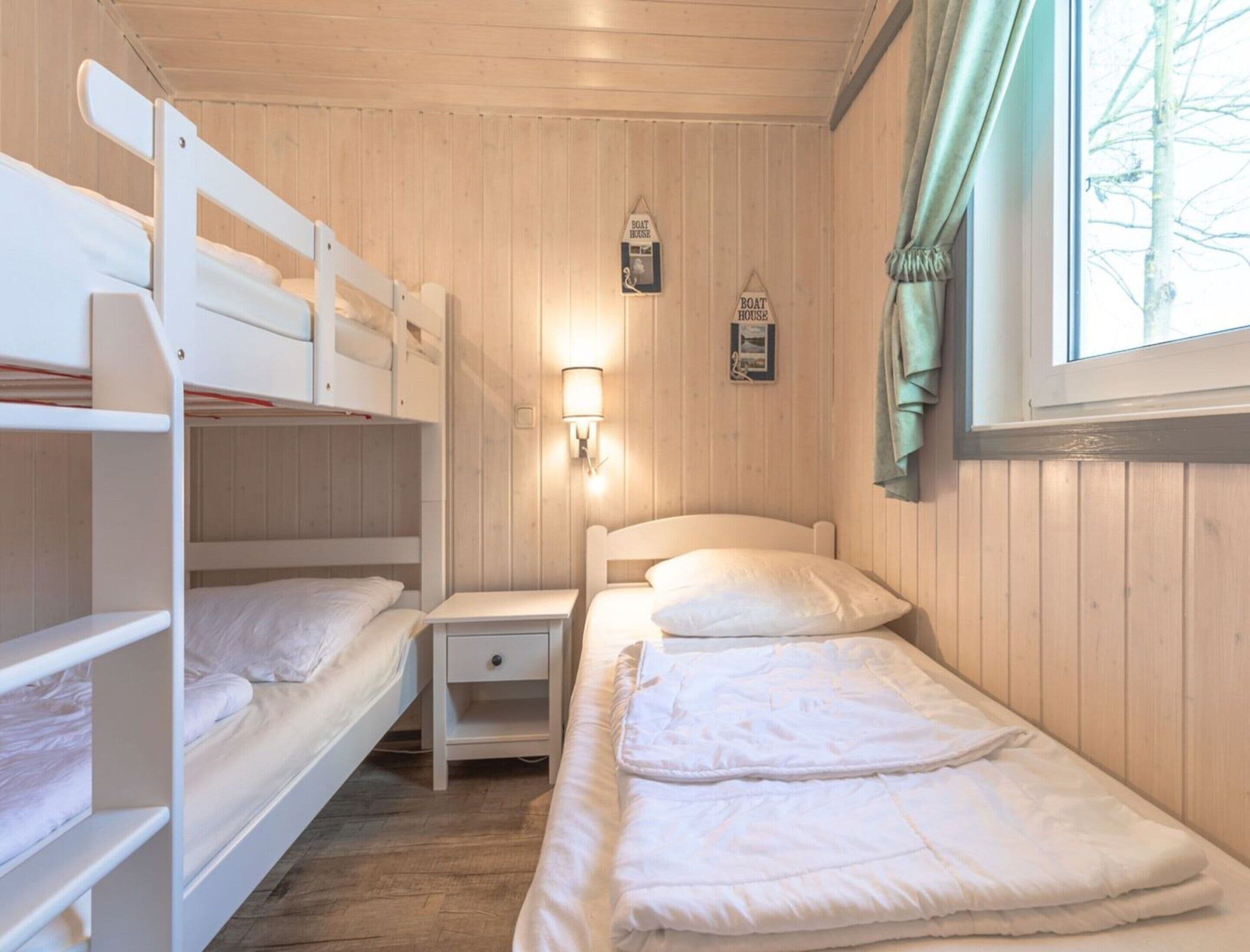 Une cabine équipée de lits superposés, d’une table de chevet, d’une lampe fixée au mur et d’une fenêtre avec des rideaux.