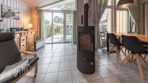 A cozy living room with a fireplace, a dining area, and a kitchen with wooden cabinets. - Ferienhaus mit Sauna im Ferienpark Mirow (Mirow)