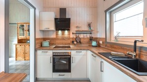 A modern kitchen with wooden paneling, a built-in oven, a sink, and a window providing natural light. - Ferienhaus mit Sauna im Ferienpark Mirow (Mirow)