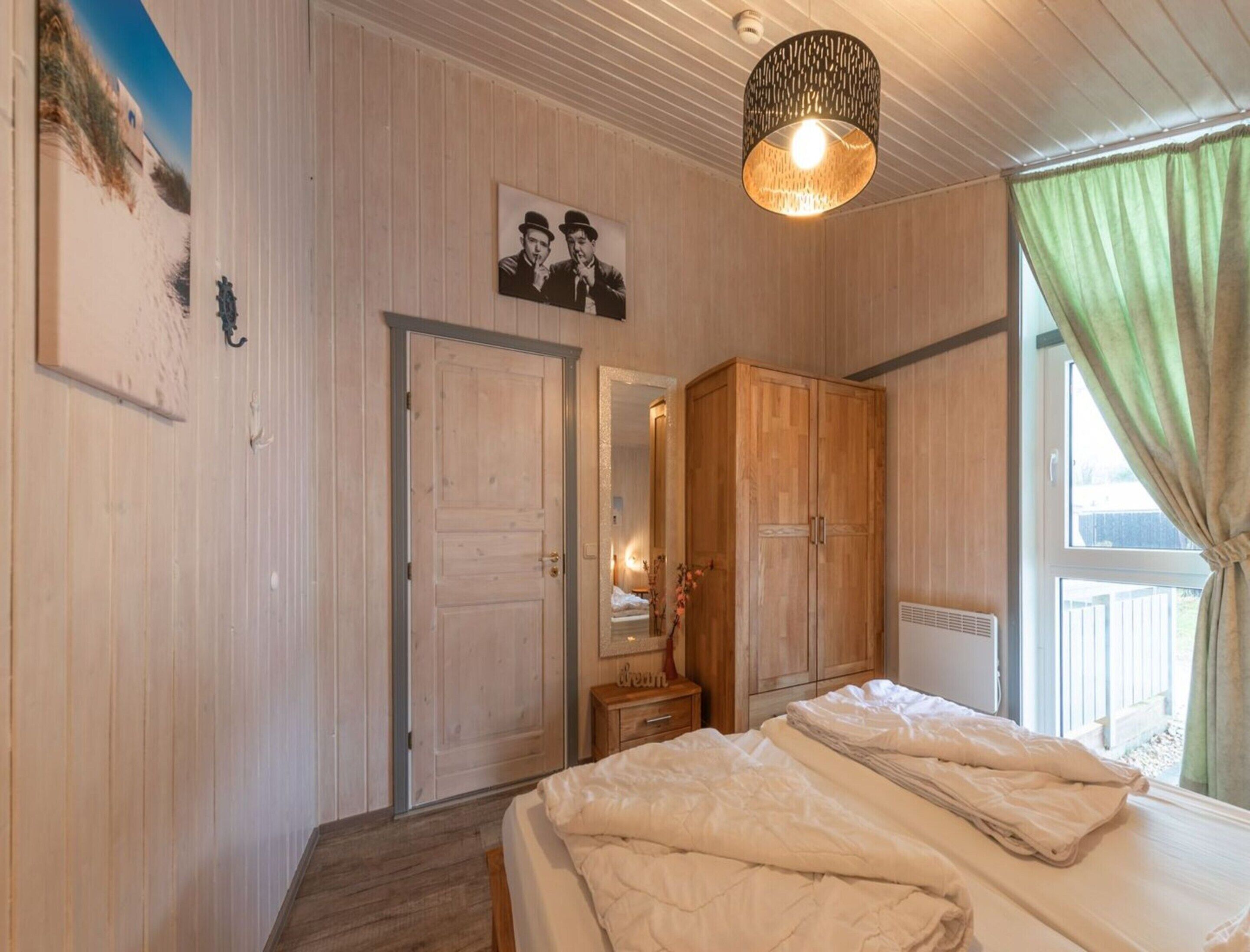 A bedroom with a bed, a wardrobe, a mirror, and a hanging light fixture.