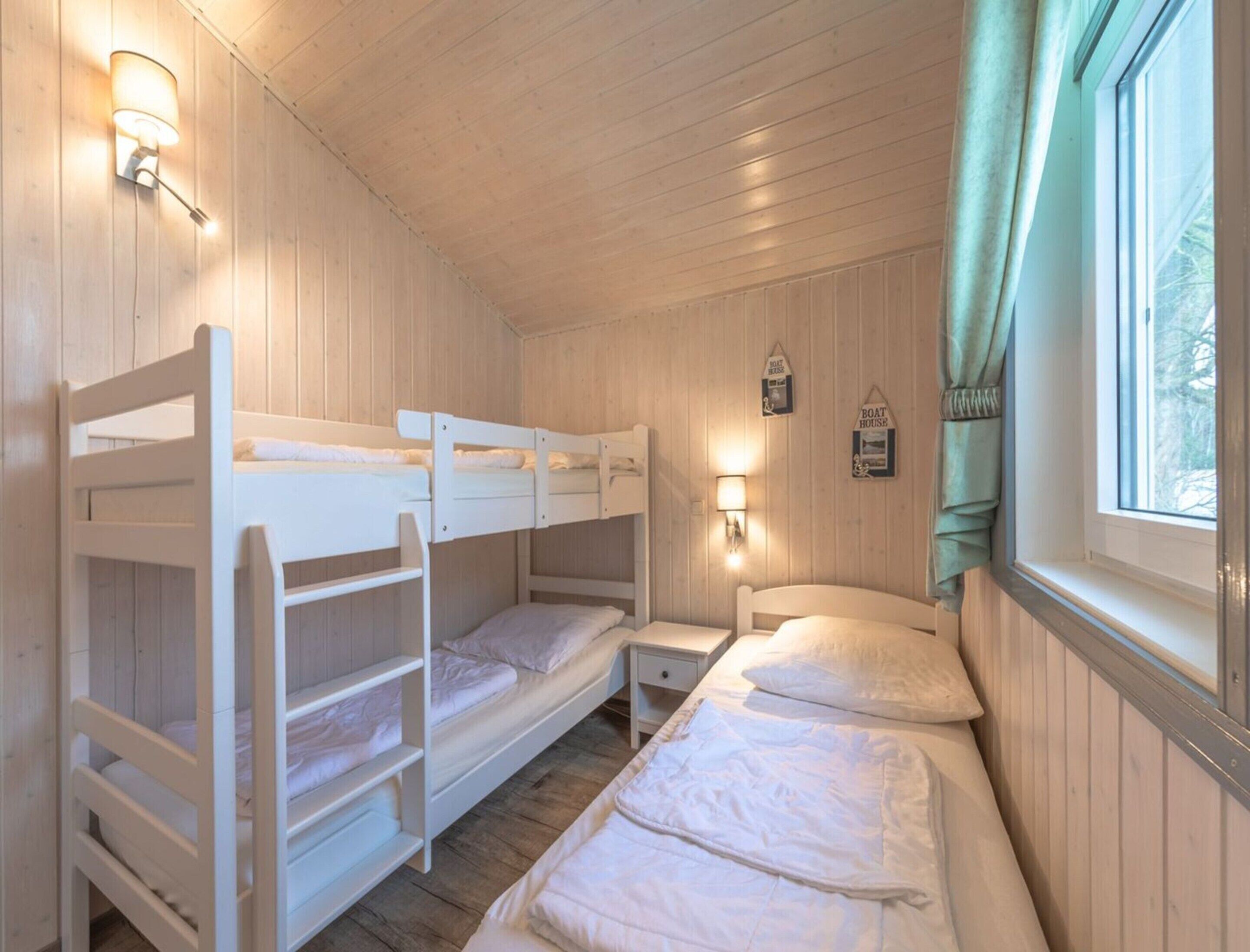 Una habitación tipo cabaña con literas, una mesita de noche pequeña y una ventana con cortinas.