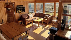 A cozy cabin interior with wooden walls, a sofa, a coffee table, and a TV mounted on the wall. - Tranquil 4-bedrooms in two cottages Near Golden Circle-10 sleeps with WiFi, AC (Grímsnes- og Grafningshreppur)