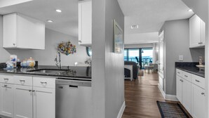 A modern kitchen with white cabinetry, a stainless steel dishwasher, and a large island with a sink. - Santa Rosa Dunes 825 (Pensacola Beach)