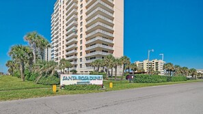 A high-rise hotel with multiple balconies, a sign for 'SANTA ROSA DUNES', and a clear blue sky. - Santa Rosa Dunes 825 (Pensacola Beach)