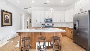 A modern kitchen with white cabinets, stainless steel appliances, and wooden stools. - Villa #17 at Bloomington Country Club: Pool, Golf, Restaurant (St. George)