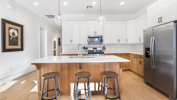 A modern kitchen with white cabinets, stainless steel appliances, and wooden stools. - Villa #17 at Bloomington Country Club: Pool, Golf, Restaurant (St. George)