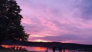 A lakeside scene with people sitting and walking near the water during sunset. - Ferienhaus mit Sauna im Ferienpark Mirow (Mirow)
