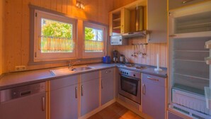 A compact kitchen with wooden cabinets, a built-in oven, a microwave, and a refrigerator. - Ferienhaus mit Sauna im Ferienpark Mirow (Mirow)