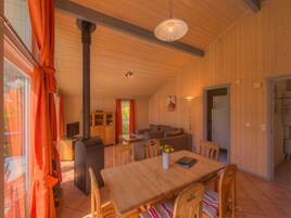 A cozy wooden interior with a dining table, chairs, a sofa, and a TV.