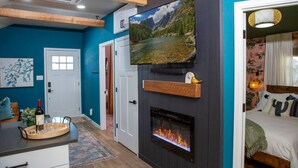 A modern living room with a fireplace, a mounted TV, and a dining area with a table set for two. - Stylish & Romantic with Hot Tub (Loveland)