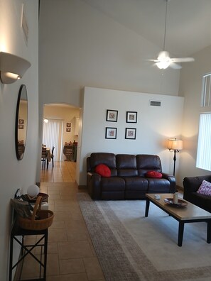 A living room with a dark leather sofa, a coffee table, a lamp, and a ceiling fan. - Spacious Stargazing Sleeps 10 Secret Gem 4BD3BA HotTub, Treadmill, Keyless Entry (Tucson)