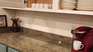 Cozinha com bancadas de granito, cafeteira e armário com copos e pratos.