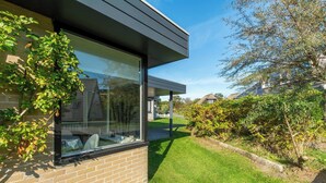 A modern house with a large glass window, a brick exterior, and a well-maintained lawn. - Bungalow in Sint Maartenszee Near Beach (Sint Maartensvlotbrug)