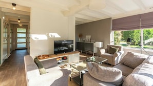 A spacious living room with a flat-screen TV, comfortable seating, and a view of the outdoors. - Bungalow in Sint Maartenszee Near Beach (Sint Maartensvlotbrug)