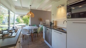 A modern kitchen with a dishwasher, a Siemens oven, and a dining area with a round table and chairs. - Bungalow in Sint Maartenszee Near Beach (Sint Maartensvlotbrug)