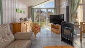 Una sala de estar acogedora con un sofá, televisor, chimenea y vistas a través de un ventanal.