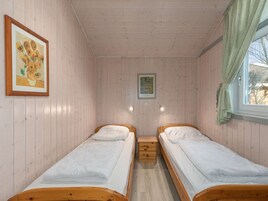Quarto com duas camas de madeira, uma pequena mesa de cabeceira, um quadro na parede e uma janela com cortinas.