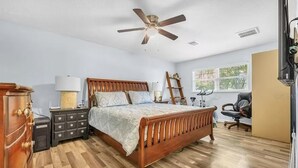 A bedroom with a wooden bed, a ceiling fan, a dresser, a desk, and a chair. - IMG, Bradenton Beach, Anna Maria, Siesta Key Beach Beautiful & Centrally Located (Sarasota)