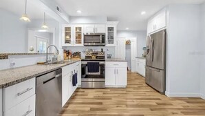 A modern kitchen with white cabinetry, stainless steel appliances, and a wooden floor. - IMG, Bradenton Beach, Anna Maria, Siesta Key Beach Beautiful & Centrally Located (Sarasota)