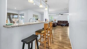 A modern kitchen with a central island, wooden bar stools, and pendant lighting. - IMG, Bradenton Beach, Anna Maria, Siesta Key Beach Beautiful & Centrally Located (Sarasota)